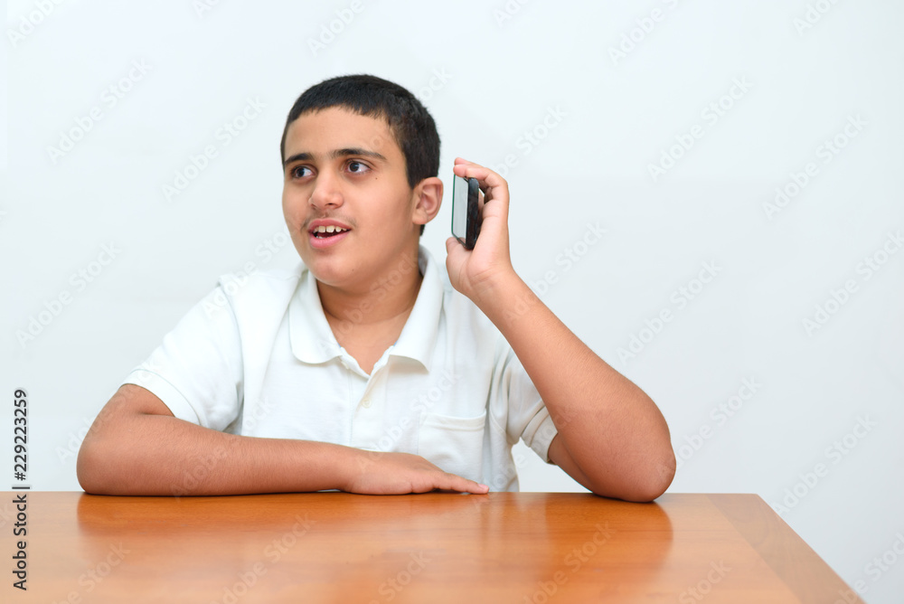 Teenager kid with mobile phone in hand sitting at wood table in home.Teen boy with deeper skin tones used his smartphone on white background in school.Young businessman talking on phone in office .