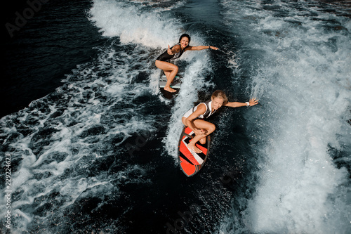 Two attractive girls riding on the wakeboard on the lake photo