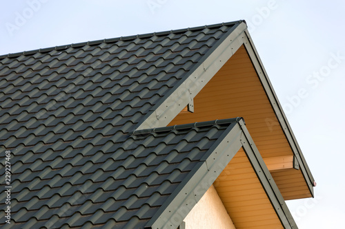 Close-up detail of new modern house top with shingled green roof on clear blue sky background. Professionally done building and construction work, real estate property, contract concept.