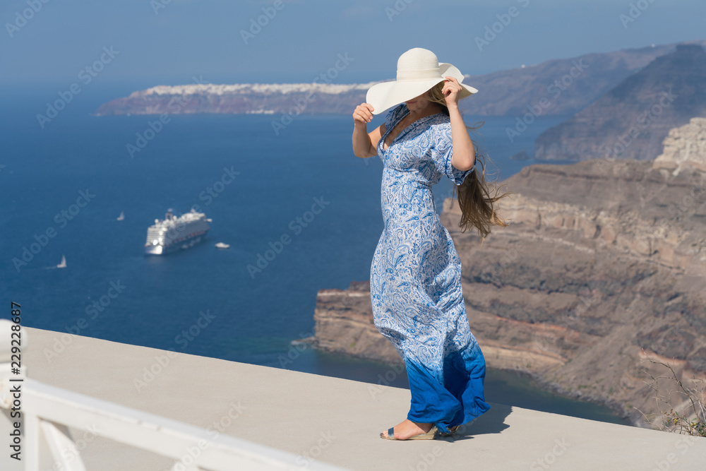 young woman in a white and blue dress enjoys a walk around Santorini