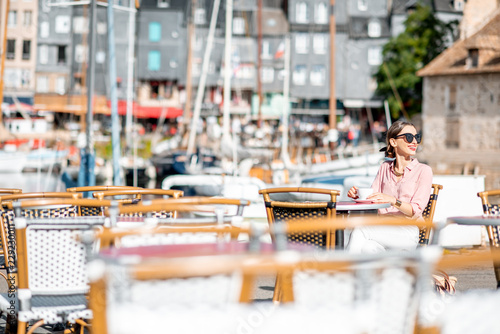 Young woman enjoying coffee sitting at the cafe outdoors near the harbour in Honfleur old town, France