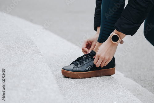 runner woman getting ready to run tying shoes laces. healthy lifestyle jogging motivation closeup of feet or footwear. fit lady wearing a digital smartwatch on hand.