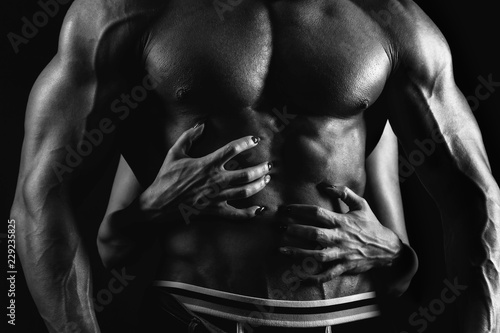 Woman is touching muscular man's torso on black background. Black and white © Peterfilm