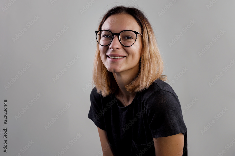 Portrait of a casual woman in big glasses and black shirt looking at camera isolated on a gray background