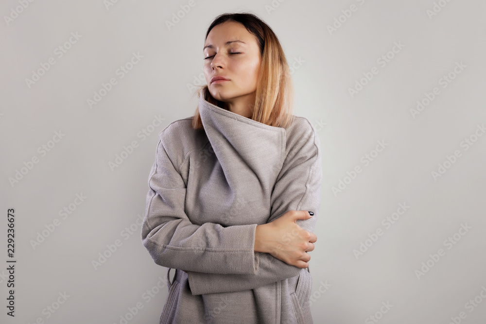 Studio portrait dreamy woman closed eyes, standing in grey coat and hug yourself over gray background Studio portrait dreamy woman closed eyes, standing in grey coat and hug yourself over gray background