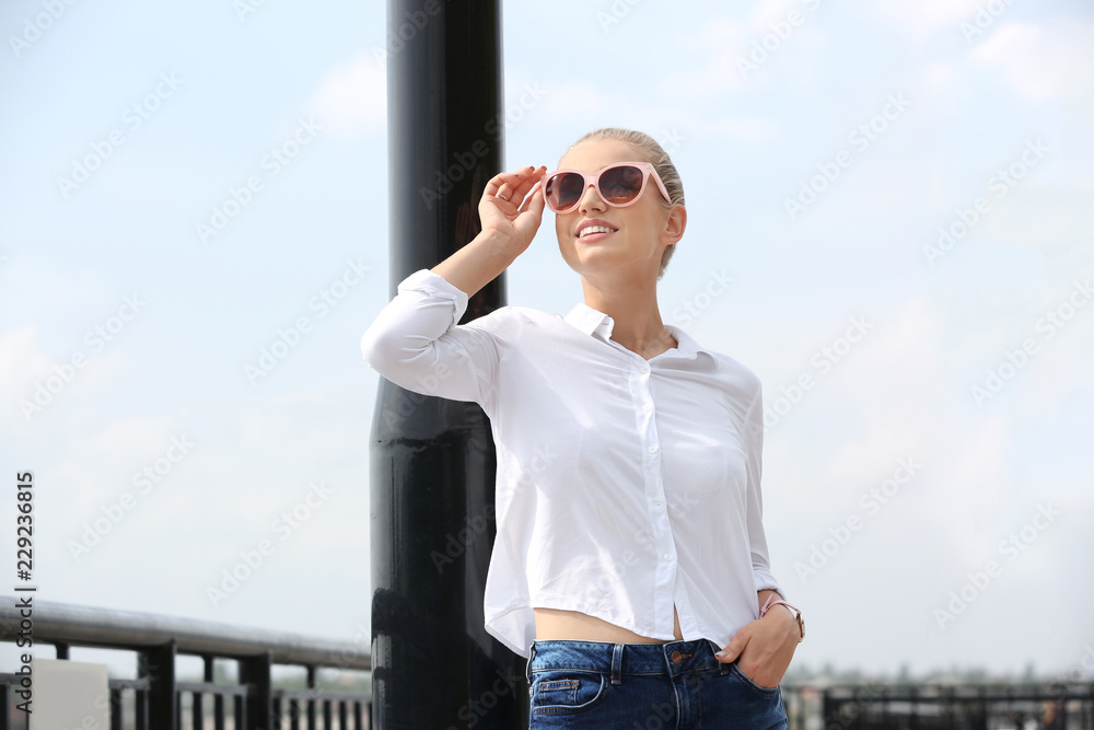 Beautiful young woman with sunglasses standing at pier. Joy in moment