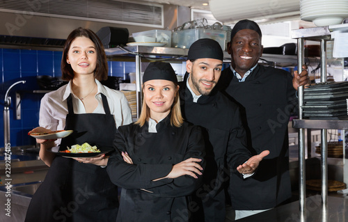 Woman waiter with command of cooks are posing together on kitchen in restaurant.