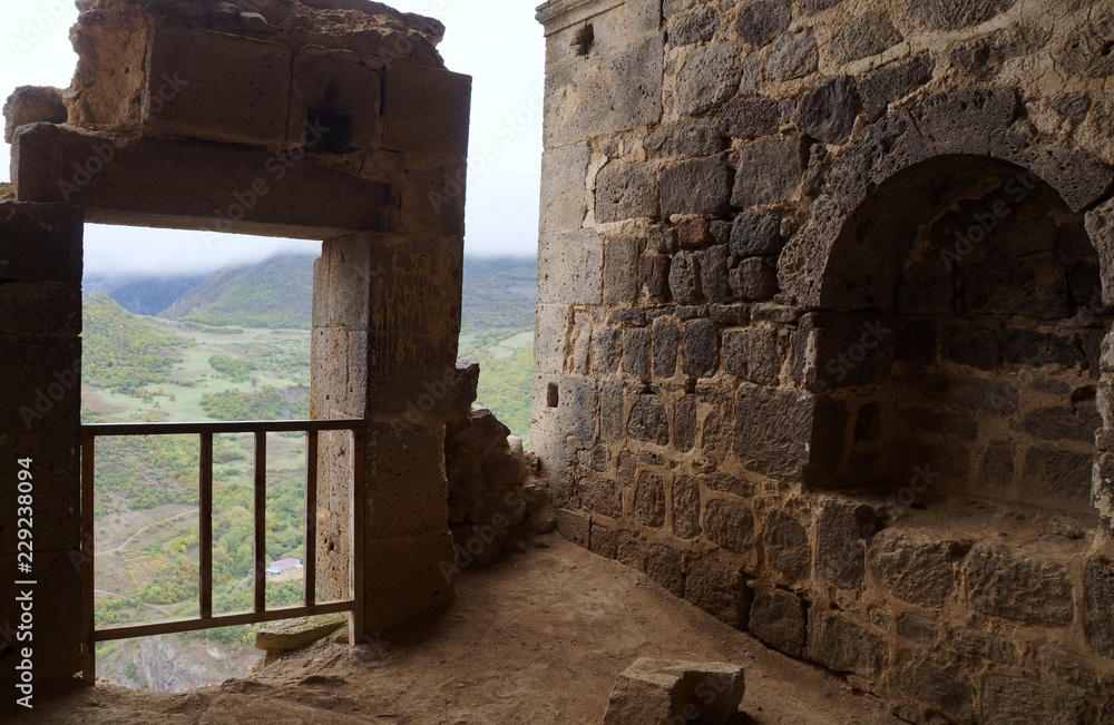 Руины старинного каменного сооружения с видом на зелёную горную долину.
