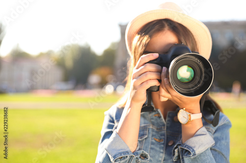Young female photographer taking photo with professional camera on street. Space for text