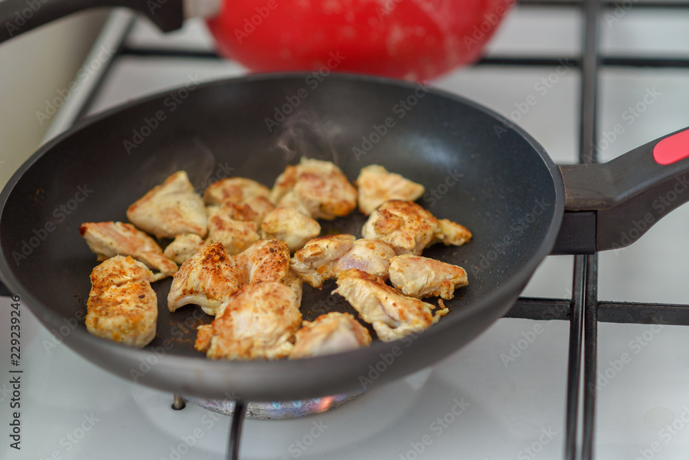 Several pieces of chopped up chicken breast with spices browned in a frying pan on stove in home.