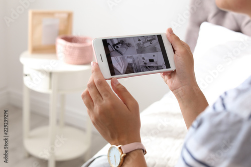 Woman monitoring modern cctv cameras on smartphone indoors, closeup