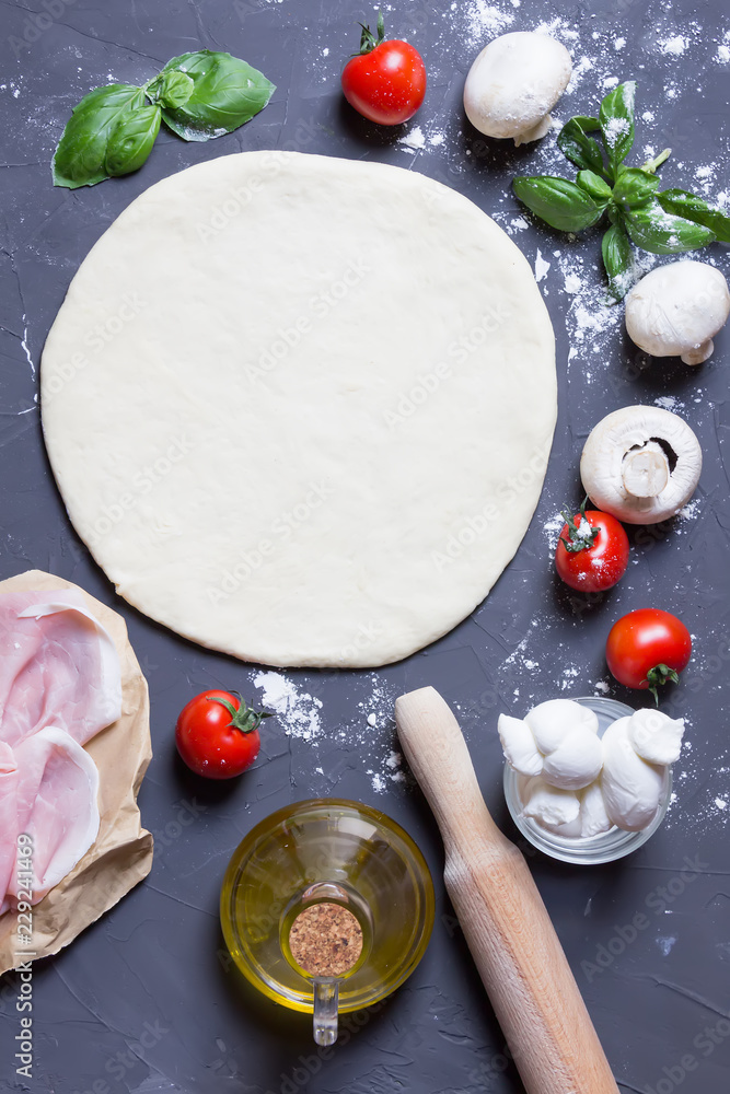 Raw dough basis with and ingredients for pizza mushrooms, tomatoes, ham, mozzarella, oil, basil on the grey background