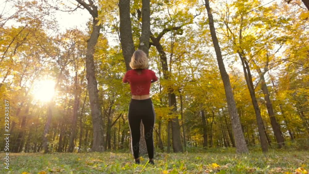 Young fit woman training with total resistance exercise system outdoors in the autumn forest. View from back. Young fit woman training with total resistance exercise system outdoors in the autumn forest. View from back.