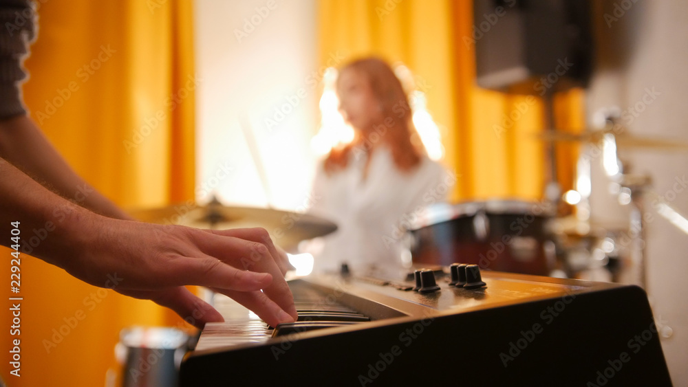 Repetition. Expressive girl drummer and a guy on keyboards. Focus from hands to drums. Backlight