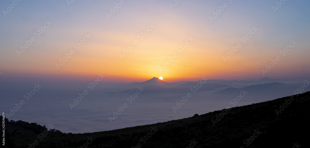 Fog in mountains. White wavy fog at the sunrise. landscape of mountains with the sun in the background