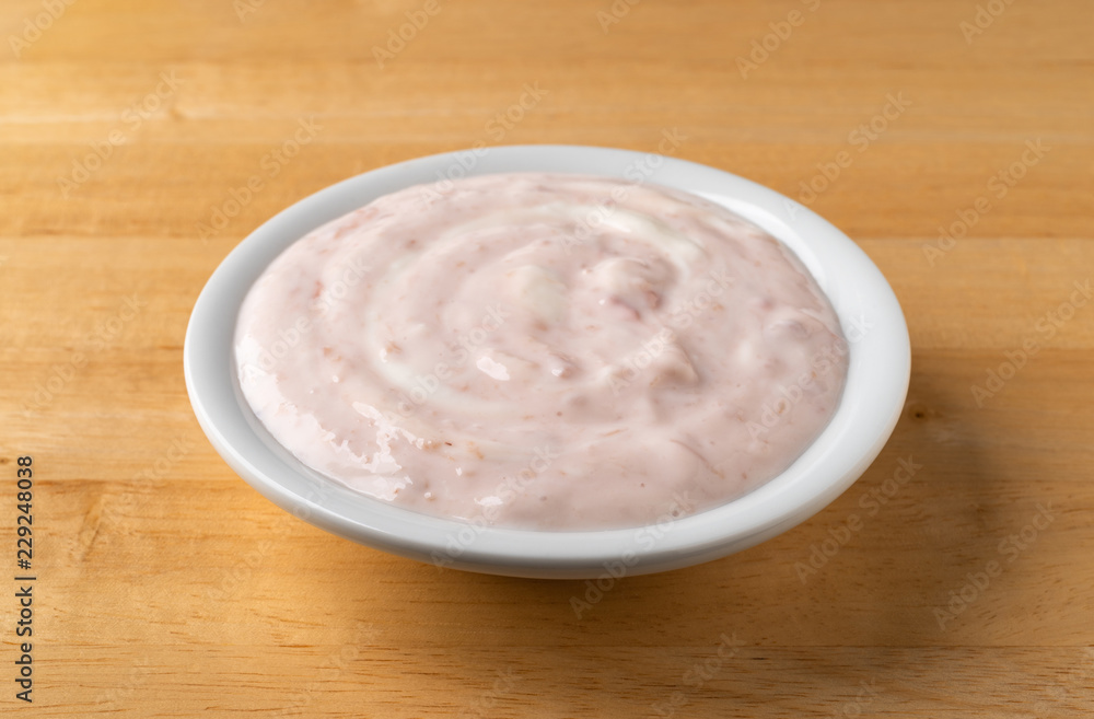 A bowl of strawberry rhubarb yogurt sweetened with honey on a wood table. A bowl of strawberry rhubarb yogurt sweetened with honey on a wood table.