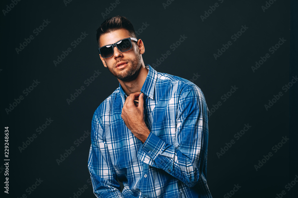 Fototapeta premium Handsome man with sunglasses posing in studio on dark background