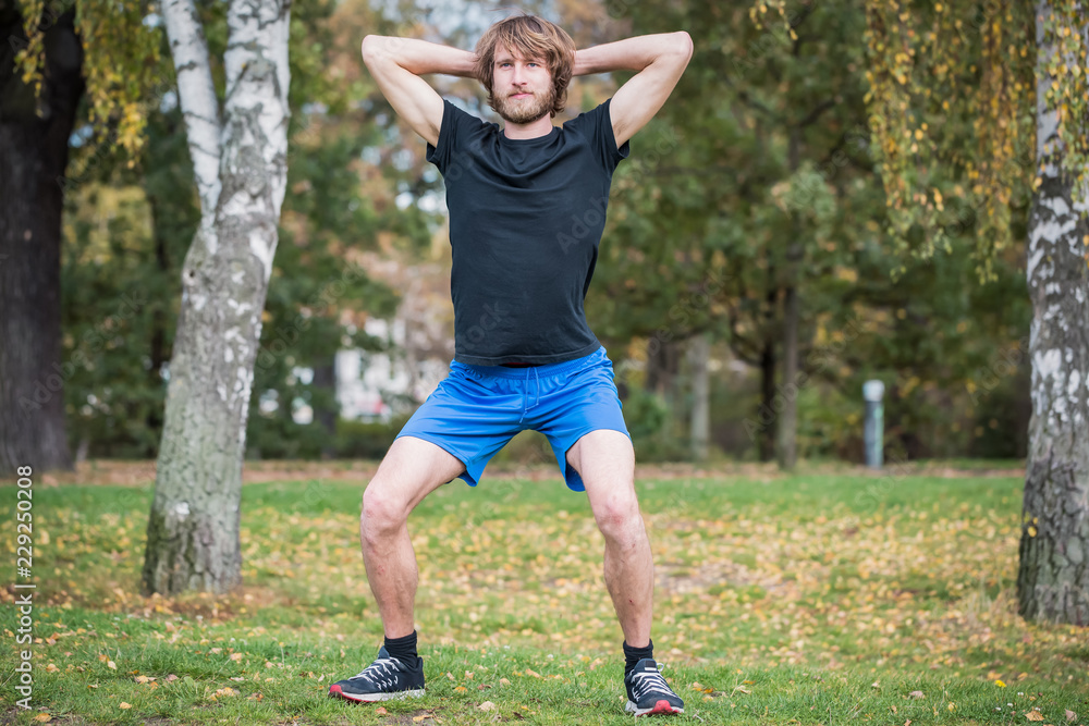 Hipster man is doing squats outdoor in the park