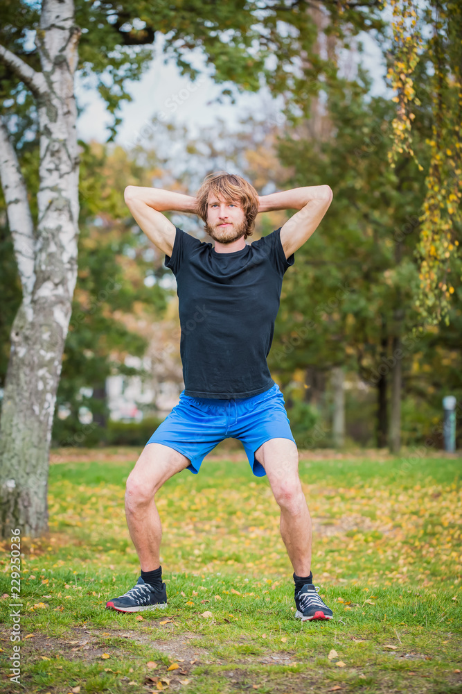 Hipster man is doing squats outdoor in the park Hipster man is doing squats outdoor in the park