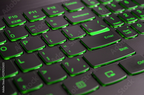 Closeup of gamer laptop keyboard green illumination, backlit keyboard, english letters