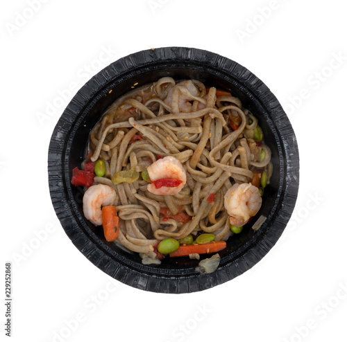 Top view of a shrimp and noodles with vegetables in a ginger sauce TV dinner in a black paper tray isolated on a white background.