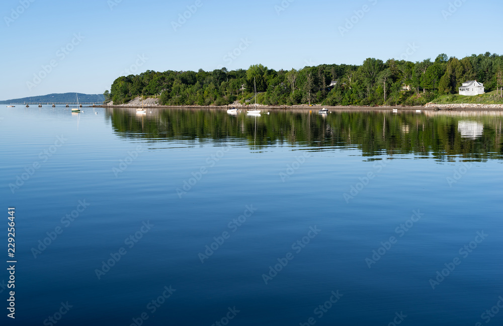View of the Penobscot Bay waterfront from the shore at  Searsport, Maine in the early morning light with bright reflections on the blue water.