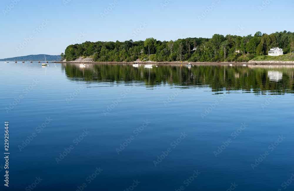 View of the Penobscot Bay waterfront from the shore at Searsport, Maine in the early morning light with bright reflections on the blue water. View of the Penobscot Bay waterfront from the shore at Searsport, Maine in the early morning light with bright reflections on the blue water.