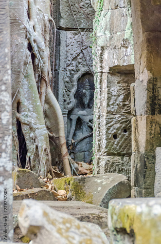 Ruins of temples of Angkor Thom with roots of a spung and the hidden female divine carved figurine photo