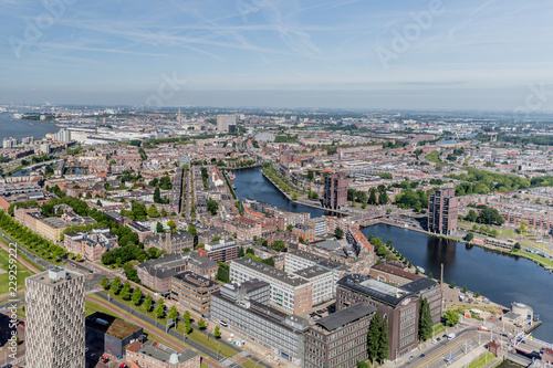 Aerial panoramic view of urban landscape of a sector of Rotterdam city with skyline in background, abundant buildings, avenue, canal and green trees, sunny day with a blue sky in the Netherlands