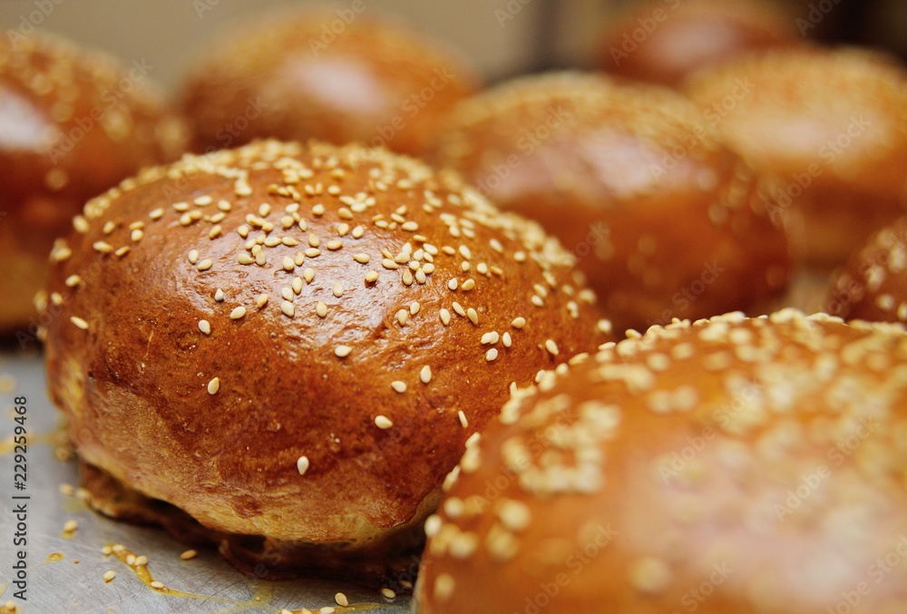 fresh appetizing buns with sesame seeds on a metal baking sheet close-up in the process of baking