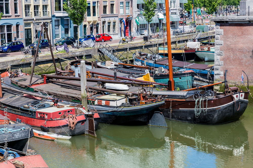 Aerial cityscape of old boats anchored at canal quay, vehicular street and buildings in background at Rotterdam city, reflection in water, sunny day for sightseeing in South Holland, Netherlands