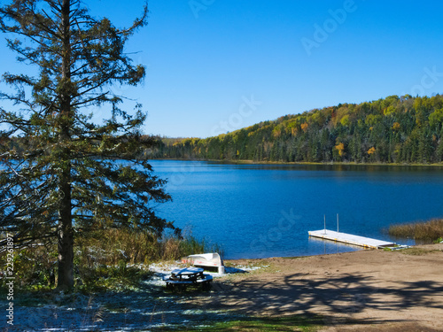 Blue sky with sunshine over beautiful serene remote northern Minnesota lake with autumn colors, boat, dock and new snow