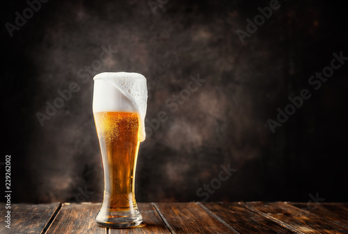 Glass of fresh and cold beer on dark background