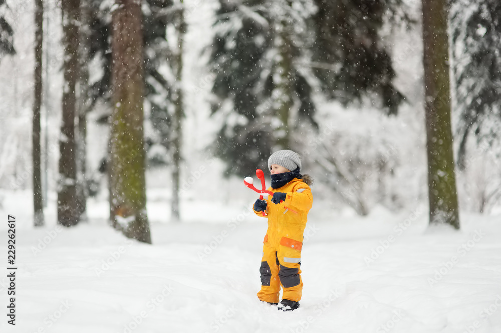 Cute little boy in yellow winter clothes walks in during a snowfall and using a plastic toy makes snowballs