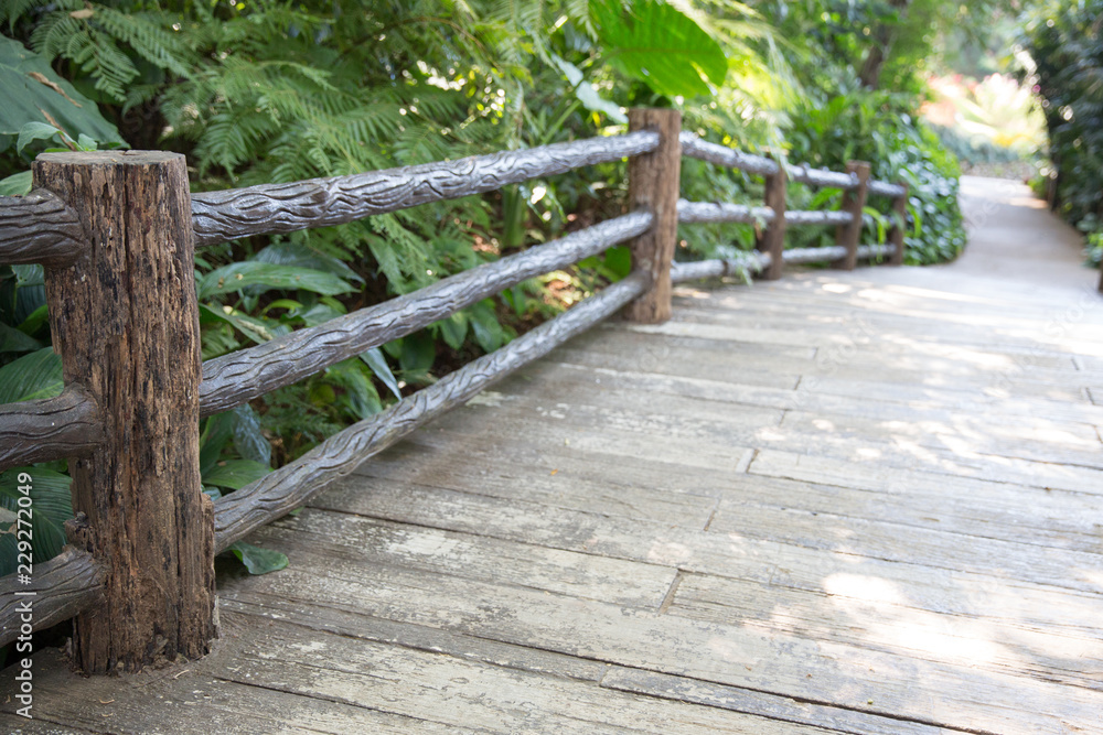 The wooden bridge as a shortcut to the wild.Wooden footbridge ropes in daylight with forest background.wooden fence with dirt road in background. The wooden bridge as a shortcut to the wild.Wooden footbridge ropes in daylight with forest background.wooden fence with dirt road in background.