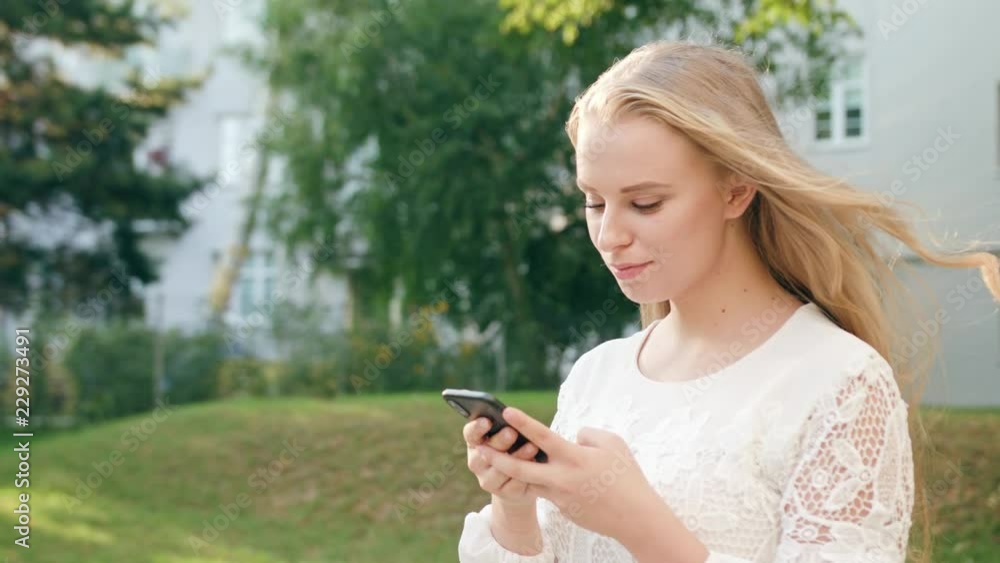 An attractive young blonde lady walking and using a phone in town. Close-up shot. Soft focus. Dolly shot An attractive young blonde lady walking and using a phone in town. Close-up shot. Soft focus. Dolly shot