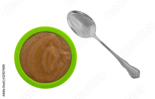 Top view of a serving of mocha instant pudding in a small green bowl with a spoon to the side isolated on a white background.