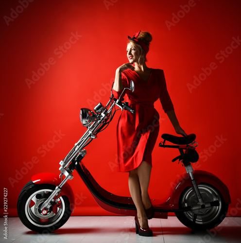 Woman ride new electric car motorcycle bicycle scooter present for new year 2019 in red dress on red background 
