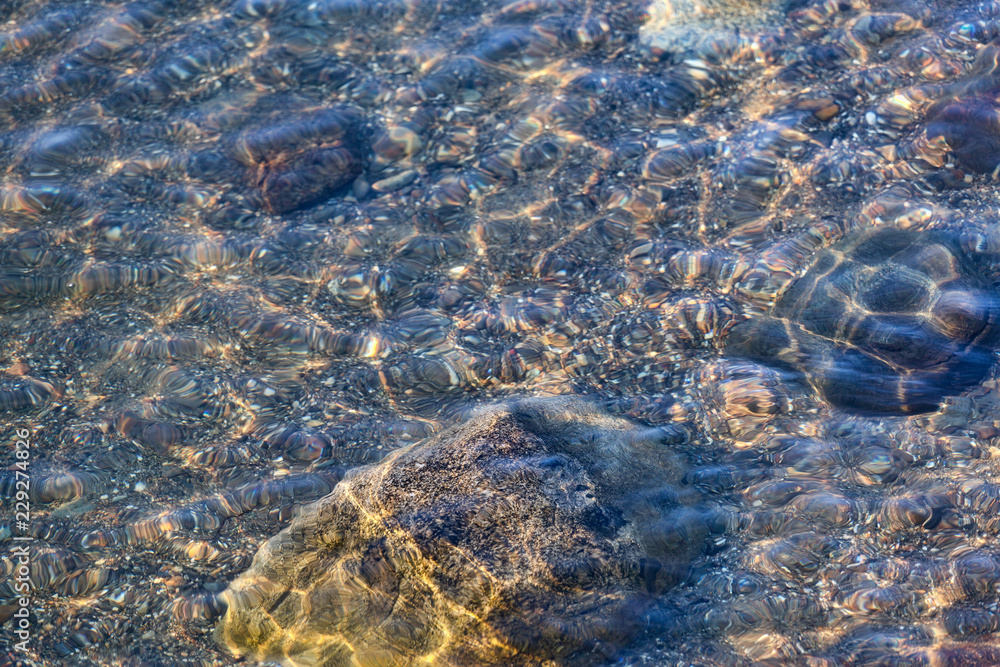 Several large rocks and gravel on the bottom of the ocean at low tied with small waves shimmering above.
