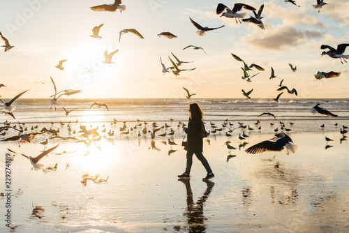 Woman walking at the beach full of seagulls at sunset, winter, Portugal