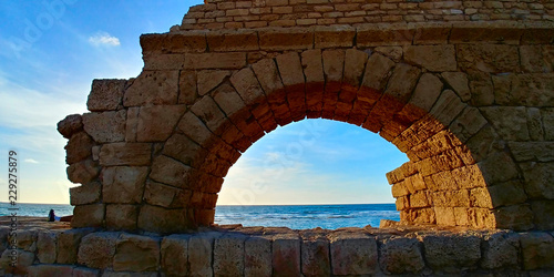 Aqueduct in Caesarea, Israel, during a sunny afternoon. The Mediterranean Sea can be seen behind the aqueduct. photo