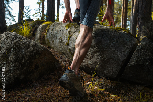 Muscled leg of the trail running athlete crossing rocky terrain in the summer forest photo
