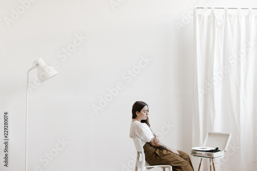 young woman sitting in big white room listening to a vinyl music record photo