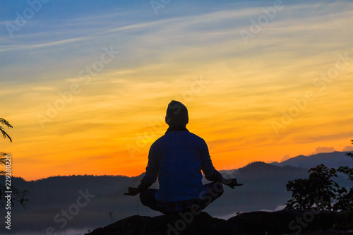 Silhouette of man doing yoga on top mountain at sunset or sunrise time