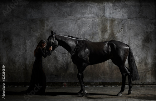 Side view of woman in black dress standing with horse in dark room photo