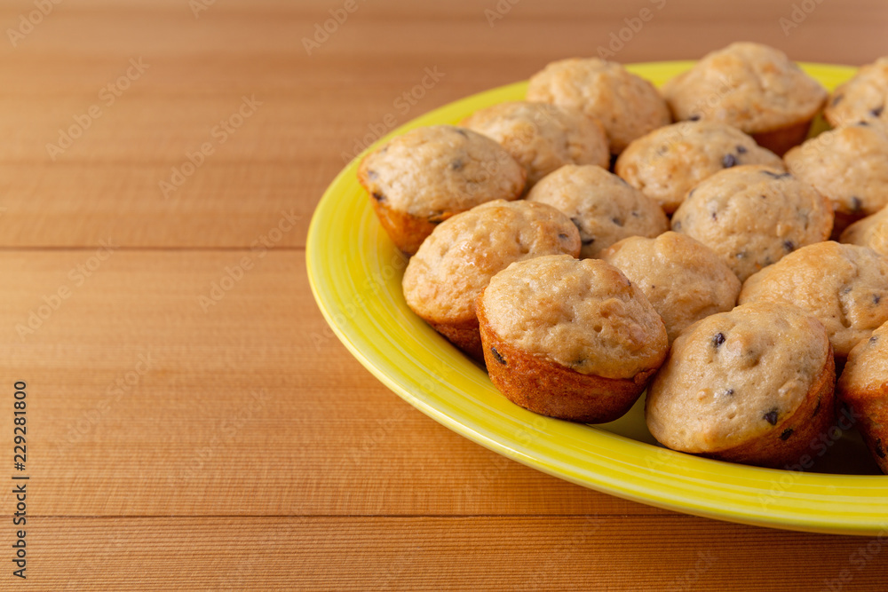 Side view of freshly baked bite size chocolate chip muffins on a yellow plate atop a wood table. Side view of freshly baked bite size chocolate chip muffins on a yellow plate atop a wood table.