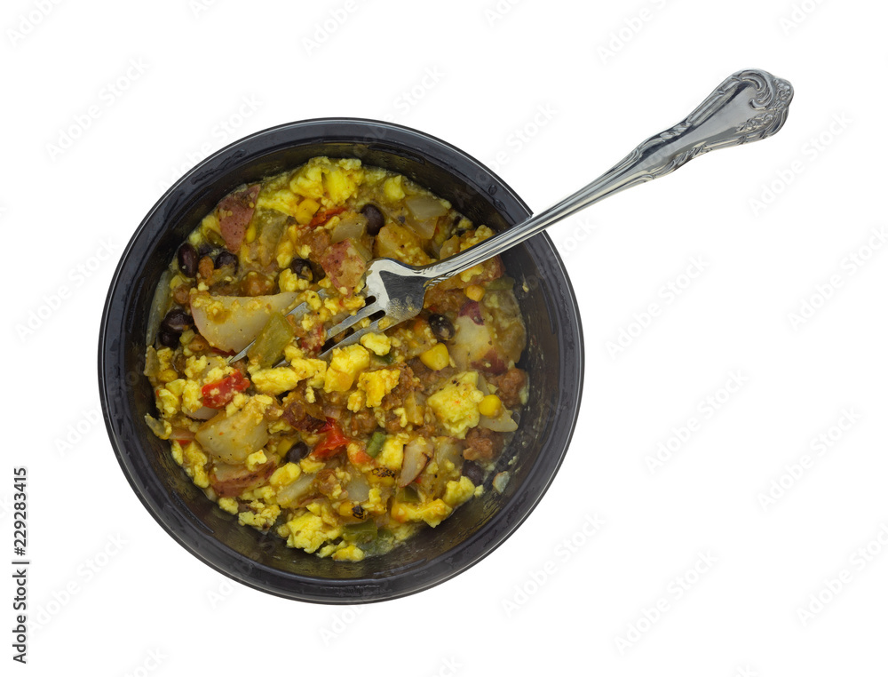 Top view of a microwaved scrambled egg burrito meal in a black tray with a fork in the food isolated on a white background.