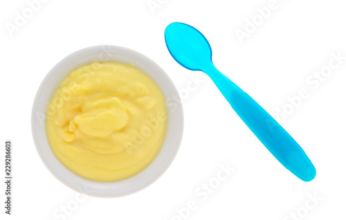 Top view of homemade banana cream pudding in a small bowl with a blue plastic spoon to the side isolated on a white background.