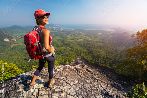 Woman hiker stands on top of the mountain and smiles and looks into camera