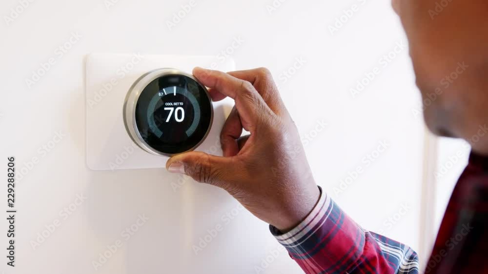 Close Up Of Man Setting Smart Heating Thermostat At Home